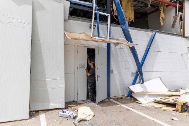 A man stands at the entrance to a factory that got hit by a missile in Petah Tikva, east of Tel Aviv, on April 3, 2026. Israel said it was under attack from a new barrage of Iranian missiles, as US President Donald Trump warned Washington had yet to begin "destroying what's left" of Iran's infrastructure. The war started more than a month ago with US-Israeli strikes on Iran, triggering retaliation that spread the conflict throughout the Middle East, convulsing the global economy and impacting millions of people worldwide. (Photo by Ilia YEFIMOVICH / AFP) / 