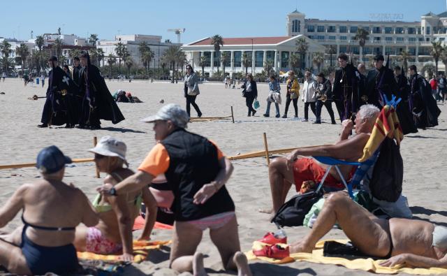 Sunbathers watch as penitents carry an effigy of the "Cristo Salvador y del Amparo" during Holy Week on the beach of Valencia on April 3, 2026. Christian believers around the world mark the holy week of easter in celebration of the crucifixion and resurrection of Jesus Christ. (Photo by Jose Jordan / AFP)