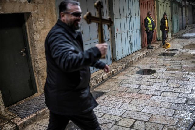 Municipal workers look on as a man walks carrying a cross along the Via Dolorosa (Way of Suffering) in the old city of Jerusalem on April 3, 2026 during the Christian Good Friday procession. (Photo by MARCO LONGARI / AFP)