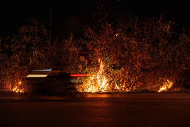 An aerial photo shows a motorist driving past a roadside wildfire in Chiang Mai on April 1, 2026. (Photo by ANTHONY WALLACE / AFP)