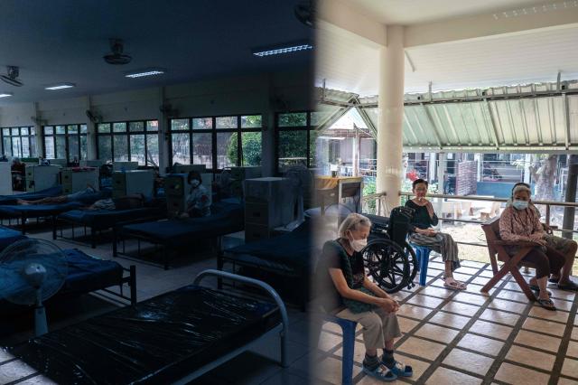 A reflection (L) on a glass door shows residents resting inside a "dust-free room”, equipped with air purifiers and positive pressure systems that keep out the polluted air, as others sit outdoors at a retirement facility in Chiang Mai on April 2, 2026. (Photo by ANTHONY WALLACE / AFP)