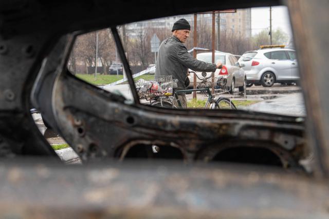 A local resident pushes his bicycle past a destroyed car at the site of an air attack in Chabany, Kyiv region on April 3, 2026, amid the Russian invasion of Ukraine. Ukraine on April 3, 2026 faced nearly 500 Russian missile and drone attacks that killed at least six people, officials said, the latest in an increasing number of daytime strikes by Moscow. (Photo by Serhii Okunev / AFP)