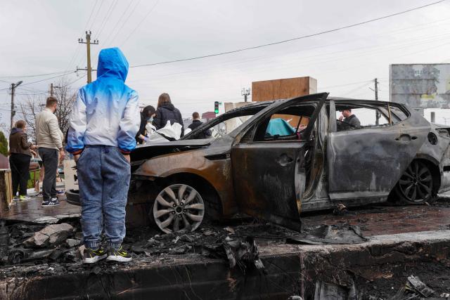 Local residents stand next to a destroyed car at the site of an air attack in Chabany, Kyiv region on April 3, 2026, amid the Russian invasion of Ukraine. Ukraine on April 3, 2026 faced nearly 500 Russian missile and drone attacks that killed at least six people, officials said, the latest in an increasing number of daytime strikes by Moscow. (Photo by Serhii Okunev / AFP)