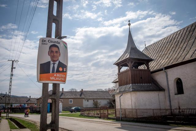 An election campaign poster of Prime Minister Viktor Orbans's Fidesz party and candidate Csuzda Gabor is pictured in the village of Bodvalenke, north-eastern Hungary, near the Hungarian-Slovak border on April 2, 2026, ahead of the country's national elections. Since 2010, the Hungarian Reformed Church Aid charity has been the main sponsor of the project 'Bodvalenke  Fresco Village': Houses in the village were painted with frescos by Roma artists from all over Hungary. The aim was to pull the village, which is mostly inhabited by Roma, out of its isolation and poverty, reduce prejudices, develop infrastructure and to turn Bodvalenke into a tourist destination. The village, a three-hour drive away from the capital Budapest, is located in one of Hungary's poorest regions. Its inhabitants pursue social work in the community or work in tourist resorts. The village has an independent mayor, yet most of the villagers show support of Prime Minister Orban's Fidesz party. The Roma are Hungary's largest minority, making up around seven percent of the 9.5 million population and often face discrimination. (Photo by FERENC ISZA / AFP)