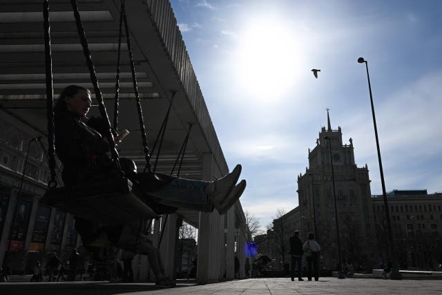 A woman rides a swing at Triumfalnaya Square with the Peking Hotel in the background in central Moscow, on April 3, 2026. (Photo by Igor IVANKO / AFP)