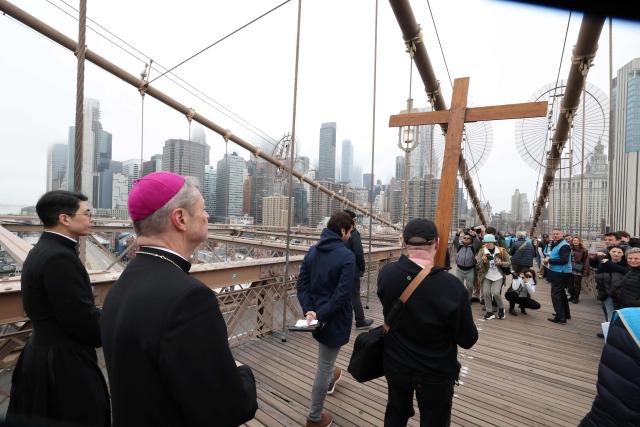 People, along with Bishop Robert Brennan (2nd L) of Brooklyn, participate in the “Way of the Cross” over the Brooklyn Bridge on Good Friday in New York on April 3, 2026. Christian believers around the world mark the Holy Week of Easter remembering the crucifixion and resurrection of Jesus Christ. (Photo by TIMOTHY A. CLARY / AFP)