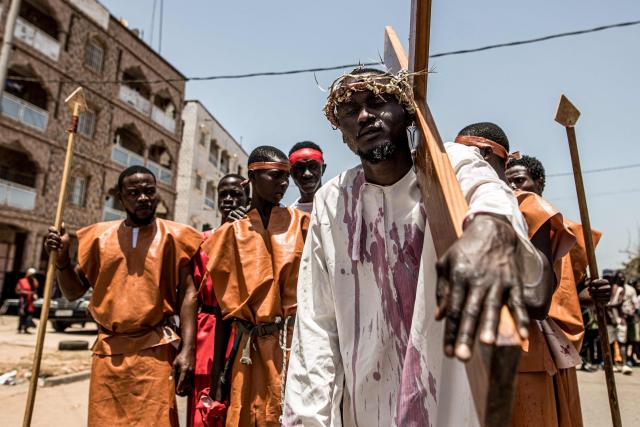 A man carries a wooden cross during a re-enactment commemorating the crucifixion of Jesus Christ, in Bakoteh, The Gambia, on April 3, 2026. (Photo by MUHAMADOU BITTAYE / AFP)