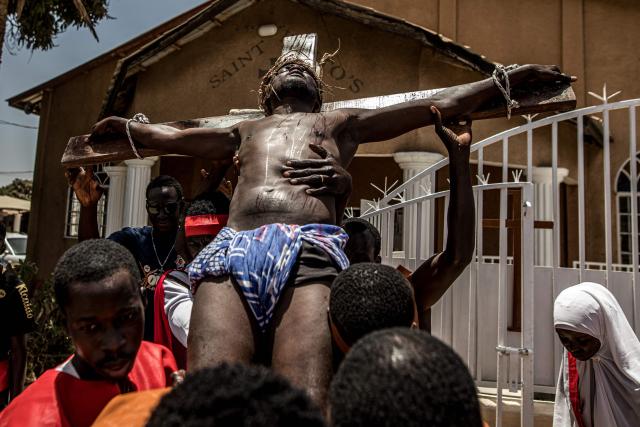 Participants carry a man tied to wooden cross during a re-enactment commemorating the crucifixion of Jesus Christ, in Bakoteh, The Gambia, on April 3, 2026. (Photo by MUHAMADOU BITTAYE / AFP)