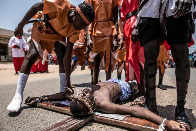 A man portraying Jesus Christ falls to the ground as he is tied to a wooden during a re-enactment commemorating the crucifixion of Jesus Christ, in Bakoteh, The Gambia, on April 3, 2026. (Photo by MUHAMADOU BITTAYE / AFP)