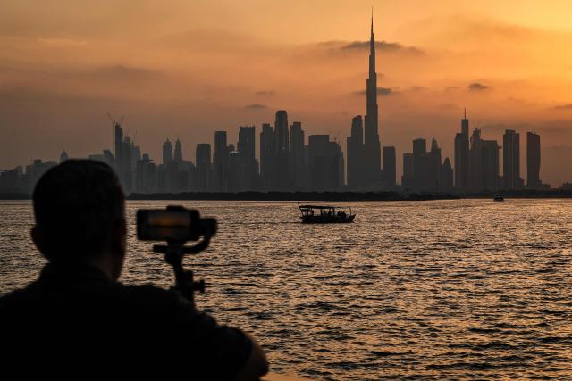 A man stands holding a smartphone in front of the Dubai skyline, with the Burj Khalifa, the world’s tallest building, seen from Creek Harbour on April 3, 2026. (Photo by FADEL SENNA / AFP)
