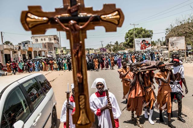 A man portraying Jesus Christ is carried on a wooden cross during a re-enactment commemorating the crucifixion of Jesus Christ, in Bakoteh, The Gambia, on April 3, 2026. (Photo by MUHAMADOU BITTAYE / AFP)