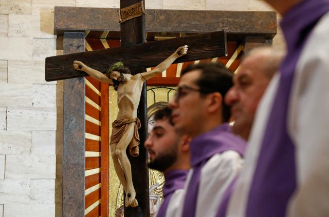 Alter boys and clergymen stand next to a crucifix during a Good Friday mass at the Our Lady of Perpetual Help Chaldean Catholic Church in Arbil, the capital of the autonomous Kurdish region of northern Iraq, on April 3, 2026. (Photo by Safin HAMID / AFP)