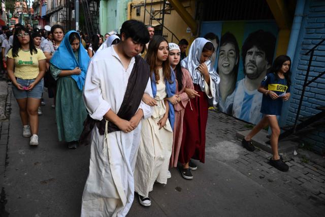 Youngsters walk past a mural depicting Argentina's football legend Diego Maradona during a procession marking the Way of the Cross on Good Friday at the Padre Carlos Mujica shantytown (known as Villa 31) in Buenos Aires on April 3, 2026. (Photo by Luis ROBAYO / AFP)