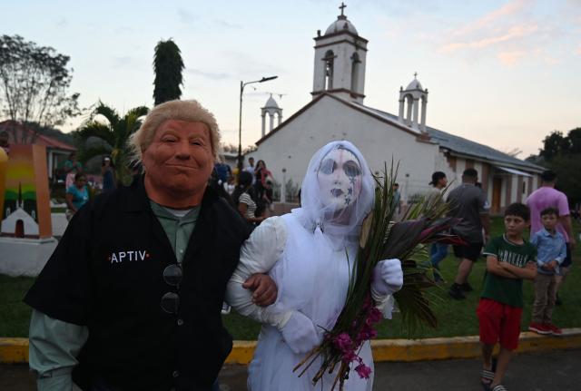 A resident with a mask depicting US President Donald Trump pretends to marry a woman with a bride's costume as part of a tradition after the Good Friday procession in Petoa, Santa Barbara department, Honduras, on April 3, 2026. (Photo by Orlando SIERRA / AFP)