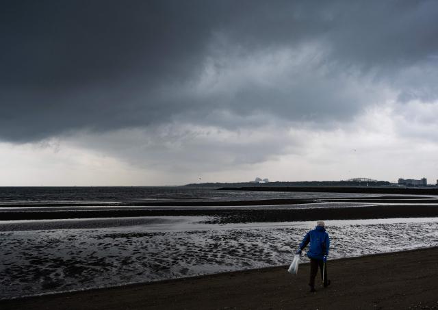 A man walks on the beach collecting trash at Kasai Rink park as a large storm moves over Tokyo on April 4, 2026. (Photo by ANDREW CABALLERO-REYNOLDS / AFP)