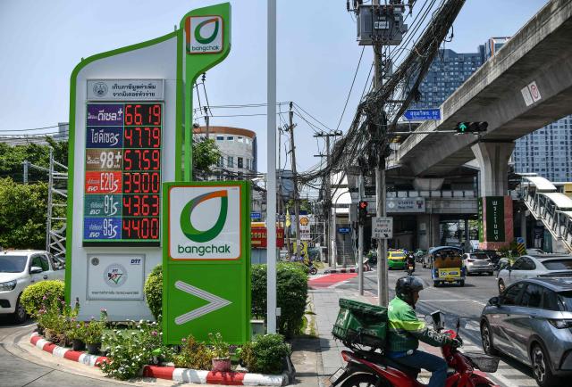 A motorcyclist rides past signage with the gas prices in Thai baht displayed at a Bangchak fuel station in Bangkok on April 4, 2026. The war in the Middle East, triggered by US and Israeli strikes on Iran on February 28, has caused disruptions to oil and gas supplies and price fluctuations across much of Southeast Asia. Fuel prices in Thailand have reached record highs, with unleaded gasoline at 57.51 baht (1.76 USD) per litre and diesel at 47.74 baht (1.46 USD). (Photo by Amaury PAUL / AFP)