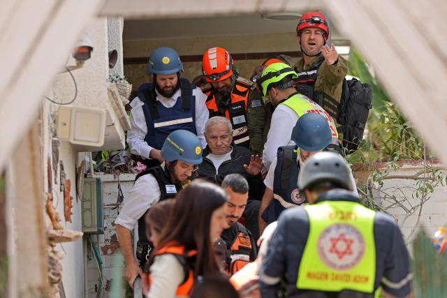Israel's first responders escort a local resident (C) from the site of an Iranian strike that hit a residential neighbourhood in Ramat Gan on April 4, 2026. The Israeli army said on April 4 its air defences were working to down missiles fired from Iran, which medics reported wounded one person. (Photo by Jack GUEZ / AFP) / 