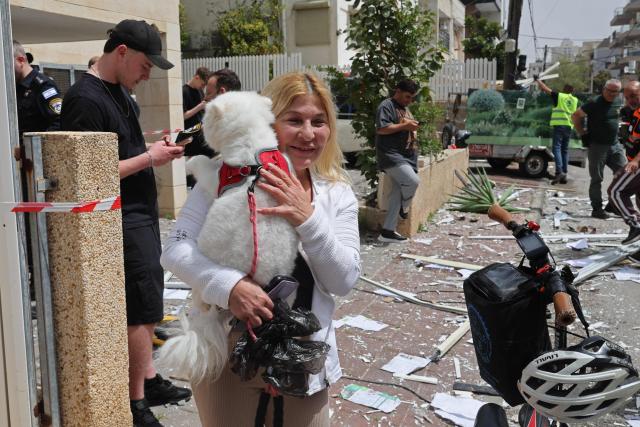 A woman carries her dog at the site of an Iranian strike that hit a residential neighbourhood in Ramat Gan on April 4, 2026. The Israeli army said on April 4 its air defences were working to down missiles fired from Iran, which medics reported wounded one person. (Photo by Jack GUEZ / AFP) / 