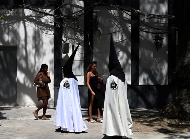 Tourists walk as penitents of the ‘El Cachorro’ brotherhood prepare to take part in Good Friday procession during Holy Week in Seville, on April 3, 2026. Christian believers around the world mark the Holy Week of Easter in celebration of the crucifixion and resurrection of Jesus Christ. (Photo by CRISTINA QUICLER / AFP)