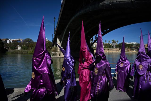 Penitents of the ‘La O’ brotherhood walk under Triana bridge before taking part in a procession during Holy Week in Seville, on April 3, 2026. Christian believers around the world mark the Holy Week of Easter in celebration of the crucifixion and resurrection of Jesus Christ. (Photo by CRISTINA QUICLER / AFP)