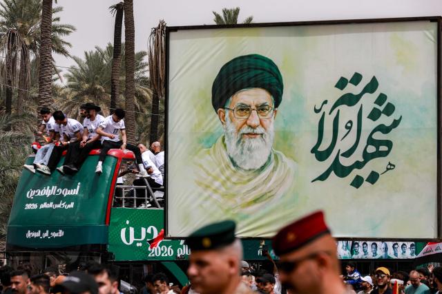 TOPSHOT - The double-decker bus carrying Iraq's men's national football team moves past a billboard depicting Iran's slain supreme leader Ayatollah Ali Khamenei in a parade with fans in the Jadriya area of central Baghdad on April 4, 2026 to celebrate the country's qualification to the 2026 FIFA World Cup to be held in North America in the summer. The "Lions of Mesopotamia" secured the country's first World Cup appearance since the 1986 competition in Mexico with a 2-1 win over Bolivia late on March 31. The build-up to the match had been overshadowed by the outbreak of the Middle East war in late February, when the US and Israel attacked Iran, subsequently dragging Iraq into the conflict. (Photo by MURTAJA LATEEF / AFP)