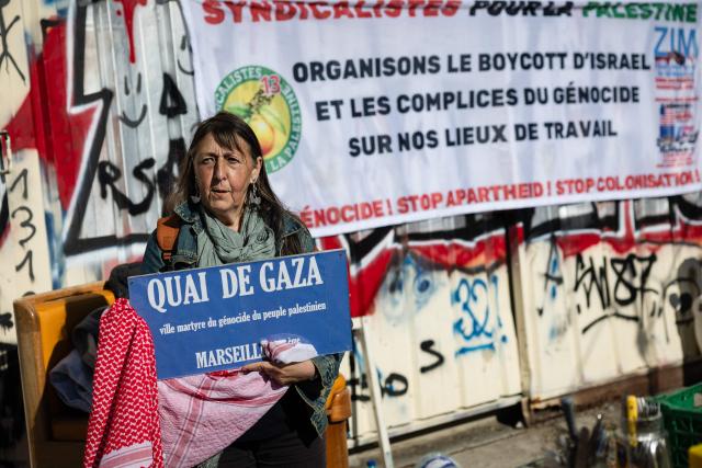 An activist holds a sign reading “Gaza Quay” in l'Estaque, part of Marseille's harbour, on April 4, 2026, during a rally in support of a flotilla carrying activists from “Thousand Madleens to Gaza” movement as they prepare to set sail. (Photo by CLEMENT MAHOUDEAU / AFP)