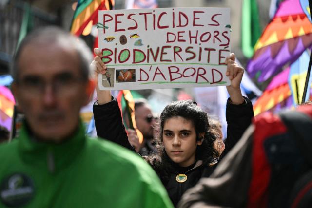 A protester raises a placard which reads "Pesticides out, biodiversity first" while taking part in the rally 'Marche Printemps Bruyant 2026', a mobilization against the use of pesticides, just a few days before World Health Day, in Paris on April 4, 2026. (Photo by Anna KURTH / AFP)