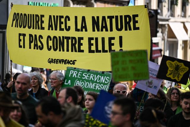 Protesters with a banner which reads "Producing with nature, not against it" take part in the rally 'Marche Printemps Bruyant 2026', a mobilization against the use of pesticides, just a few days before World Health Day, in Paris on April 4, 2026. (Photo by Anna KURTH / AFP)