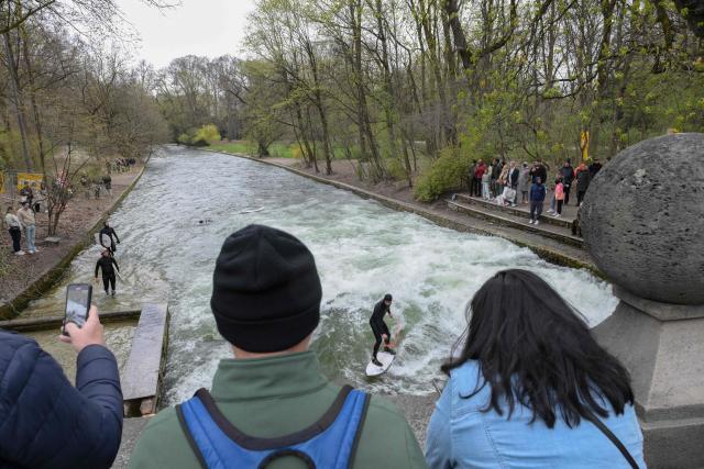 People watch as surfers return to the famous Eisbach wave (Eisbachwelle) in the English Garden (Englischer Garten) in Munich, southern Germany, on April 4, 2026. The Eisbach wave, beloved by surfers worldwide, was flattened following river cleaning operations, authorities announced on November 4, 2025 and is now set to return. (Photo by Markus FISCHER / AFP)