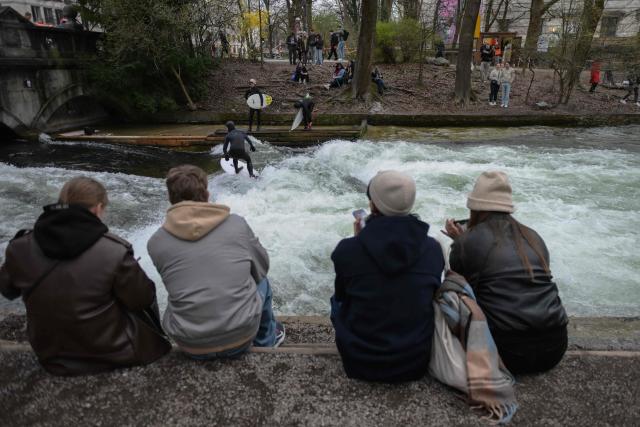Surfers check out the famous Eisbach wave (Eisbachwelle) in the English Garden (Englischer Garten) in Munich, southern Germany, on April 4, 2026. The Eisbach wave, beloved by surfers worldwide, was flattened following river cleaning operations, authorities announced on November 4, 2025 and is now set to return. (Photo by Markus FISCHER / AFP)