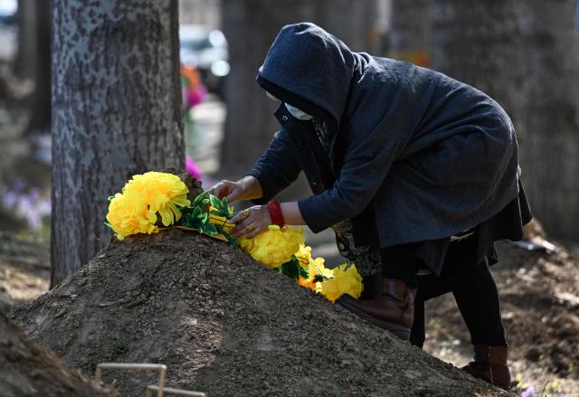 A woman decorates the grave of a family member during the annual tomb-sweeping festival, also known as the Qingming festival, near a village east of Beijing on April 5, 2026. (Photo by GREG BAKER / AFP)