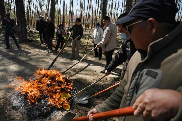 Family members burn paper as they pay their respects at the grave of their ancestor during the annual tomb-sweeping festival, also known as the Qingming festival, near a village east of Beijing on April 5, 2026. (Photo by GREG BAKER / AFP)