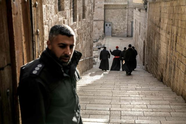 TOPSHOT - An Israeli policeman (L) looks on as Cardinal Pierbattista Pizzaballa (3rd-L), Latin Patriarch of Jerusalem, gestures as he arrives accompanied by other Franciscan Friars to the Church of the Holy Sepulcre for the Easter Sunday Mass, behind closed doors due to the ongoing war, in the old city of Jerusalem on April 5, 2026. (Photo by MARCO LONGARI / AFP)