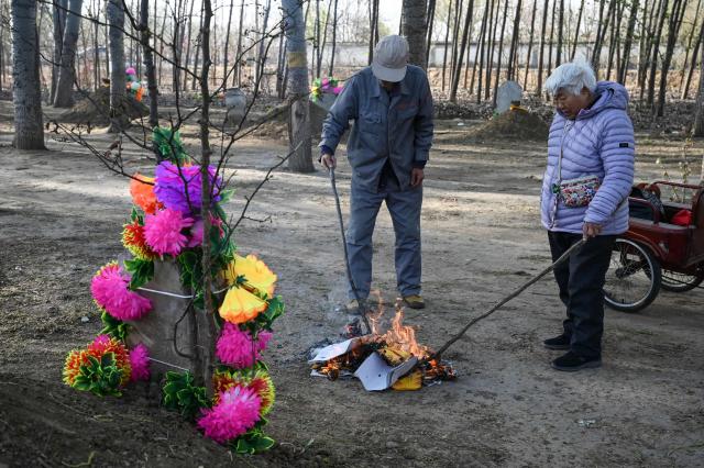 People burn paper to pay their respects at the grave of a family member during the annual tomb-sweeping festival, also known as the Qingming festival, near a village east of Beijing on April 5, 2026. (Photo by GREG BAKER / AFP)