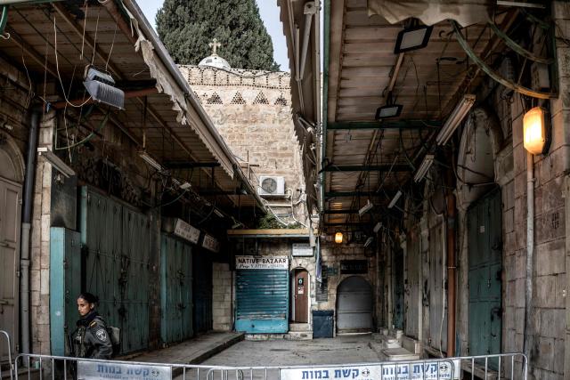 TOPSHOT - An Israeli border guard stands behind a security barrier at the entrance of the Church of the Holy Sepulchre where the Latin Patriarch of Jerusalem will celebrate Easter Sunday Mass, behind closed doors due to the ongoing war, in the old city of Jerusalem on April 5, 2026. (Photo by MARCO LONGARI / AFP)