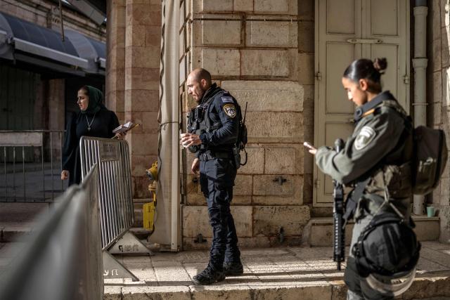A Christian Orthodox pilgrim (L) looks on while leaning against a security barrier near an Israeli policeman and a border guard near the entrance of the Church of the Holy Sepulchre where the Latin Patriarch of Jerusalem will celebrate Easter Sunday Mass, behind closed doors due to the ongoing war, in the old city of Jerusalem on April 5, 2026. (Photo by MARCO LONGARI / AFP)