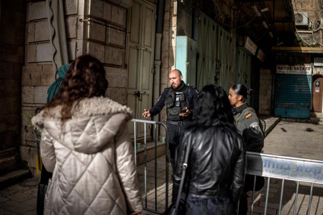 An Israeli policeman (C) explains from behind a security barrier to a group of Orthodox Christian pilgrims that they are not allowed to the Church of the Holy Sepulchre, where the Latin Patriarch of Jerusalem will celebrate Easter Sunday Mass, behind closed doors due to the ongoing war, in the old city of Jerusalem on April 5, 2026. (Photo by MARCO LONGARI / AFP)