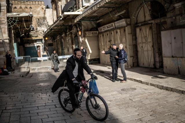 An Orthodox Jewish man rides his bicycle as an Israeli policeman (2nd-R) argues with a Christian pilgrim who is refused entry to the Church of the Holy Sepulchre, where the Latin Patriarch of Jerusalem will celebrate Easter Sunday Mass, behind closed doors due to the ongoing war, in the old city of Jerusalem on April 5, 2026. (Photo by MARCO LONGARI / AFP)