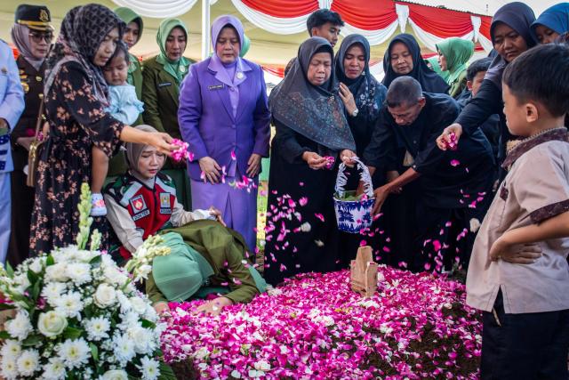 Fafa Nur Aziila (kneeling 2nd L), the widow of fallen Indonesian soldier and UN peacekeeper Farizal Rhomadhon, cries over his grave as family members scatter flower petals during his funeral at the Giripeni Heroes' Cemetery in Kulon Progo, Yogyakarta, on April 5, 2026. Farizal was one of three Indonesian soldiers killed while serving with the United Nations Interim Force in Lebanon (UNIFIL) in southern Lebanon, where Israel and Hezbollah have been fighting since Lebanon was drawn into the Middle East war. (Photo by DEVI RAHMAN / AFP)