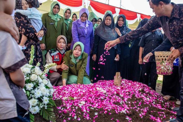 Fafa Nur Aziila (kneeling 2nd L), the widow of fallen Indonesian soldier and UN peacekeeper Farizal Rhomadhon, cries over his grave as family members scatter flower petals during his funeral at the Giripeni Heroes' Cemetery in Kulon Progo, Yogyakarta, on April 5, 2026. Farizal was one of three Indonesian soldiers killed while serving with the United Nations Interim Force in Lebanon (UNIFIL) in southern Lebanon, where Israel and Hezbollah have been fighting since Lebanon was drawn into the Middle East war. (Photo by DEVI RAHMAN / AFP)