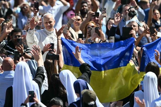 Pope Leo XIV waves to the crowd from the popemobile as people wave Ukrainian flags after the Easter Mass as part of the Holy Week celebrations, at St Peter's square in the Vatican on April 5, 2026. (Photo by Alberto PIZZOLI / AFP)