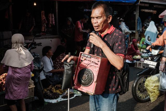A visually impaired man sings while walking with a white cane and a speaker hanging from his neck in Jakarta on April 4, 2026. (Photo by YASUYOSHI CHIBA / AFP)