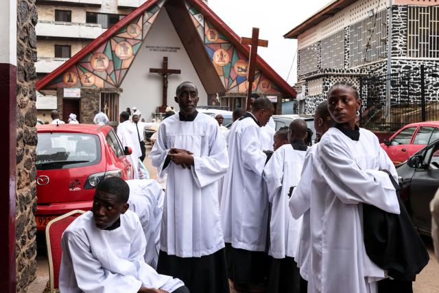 Altar servers look on as they gather in the courtyard of Notre Dame des Victoires Cathedral before the start of Easter Mass in Yaounde on April 5, 2026. (Photo by Daniel BELOUMOU OLOMO / AFP)