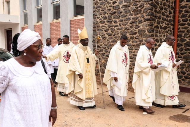 Archbishop of Yaounde Jean Mbarga (C) walks through the courtyard of Notre Dame des Victoires Cathedral before the start of Easter Mass in Yaounde on April 5, 2026. (Photo by Daniel BELOUMOU OLOMO / AFP)