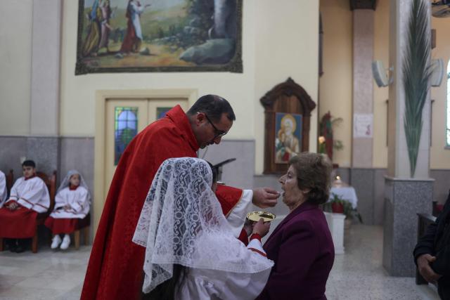 A worshipper receives communion from Father Bashar Fawadleh during the Palm Sunday mass at the Latin Church in the mostly Christian town of Taybeh, in the Israeli-occupied West Bank on Orthodox Palm Sunday on April 5, 2026. (Photo by Zain JAAFAR / AFP)
