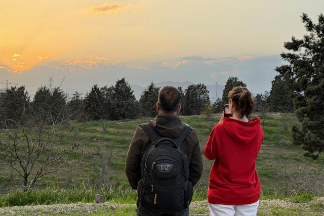 A couple takes pictures of the sunset at the Pardisan Park in Tehran on April 5, 2026. The war, which erupted on February 28, 2026 with US-Israeli strikes on Iran, has engulfed the Middle East and convulsed the global economy. (Photo by ATTA KENARE / AFP)