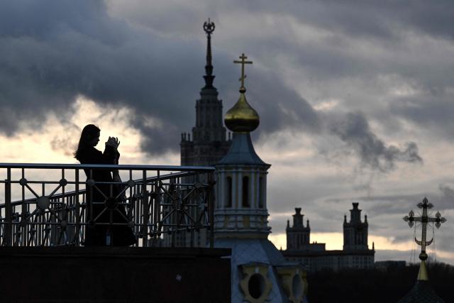 A woman takes a picture with a smartphone on an observation deck near the Russian Academy of Sciences overlooking the Moscow State University buildind and Saint Andrew's Church in Moscow, on April 5, 2026. (Photo by Igor IVANKO / AFP)