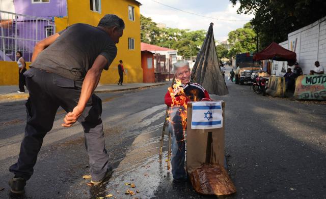 A man sets fire to an effigy depicting US President Donald Trump and an Israeli flag during the Burning of Judas ritual as part of Easter celebrations on a street in the 23 de Enero neighborhood in Caracas on April 5, 2026. (Photo by Jesus VARGAS / AFP)
