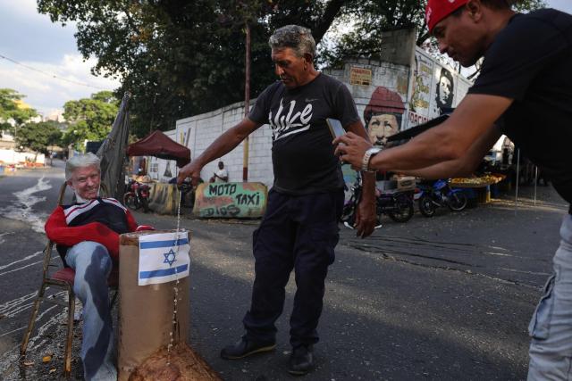 A man pours alcohol on an effigy depicting US President Donald Trump and an Israeli flag during the Burning of Judas ritual as part of Easter celebrations on a street in the 23 de Enero neighborhood in Caracas on April 5, 2026. (Photo by JESUS VARGAS / AFP)