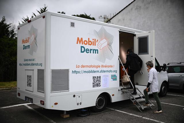 Dermatologist Blandine De Carrere (R) and a patient step into an itinerant truck for an appointment as part of the Mobil Derm project supported by the Societe Francaise de Dermatologie (French Dermatology Society) at a parking lot in Lafox, south-western France, on April 2, 2026. As in the rest of France, patients suffering from skin diseases are facing significant delays in receiving care in Nouvelle-Aquitaine, with loss of chances in the most serious cases. In Lafox, 25 patients a day enter the few square meters of the mobile clinic, where a dermatologist from the Basque Country has come for two days to carry out consultations in her free time  a pioneering system in France intended to compensate for the shortage of dermatologists and address medical deserts. (Photo by Christophe ARCHAMBAULT / AFP)